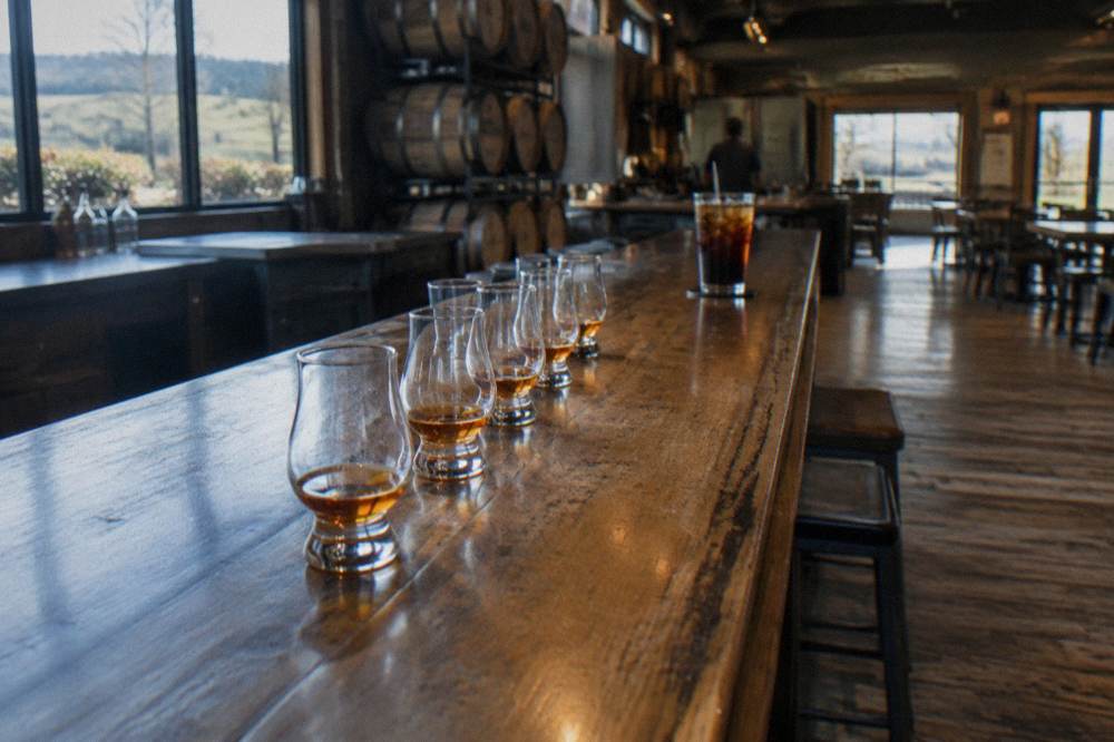 A line of small tasting glasses on a wooden bar top in a distillery tasting room