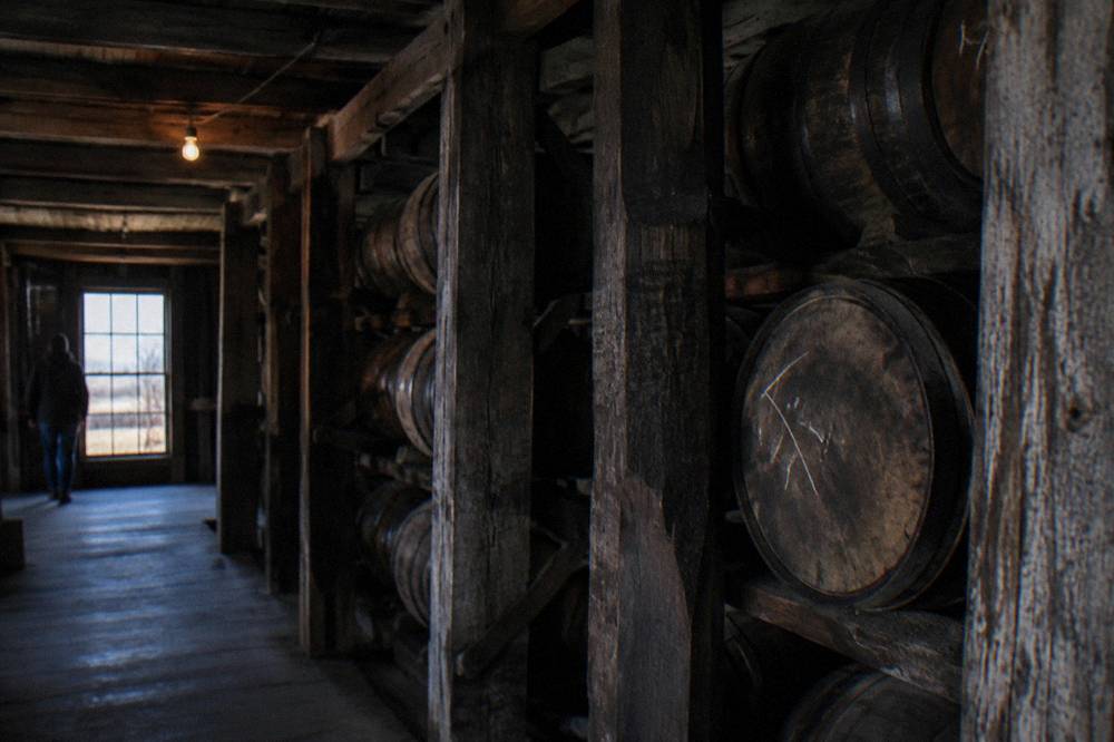 Wooden bourbon barrels stacked inside a dim rickhouse