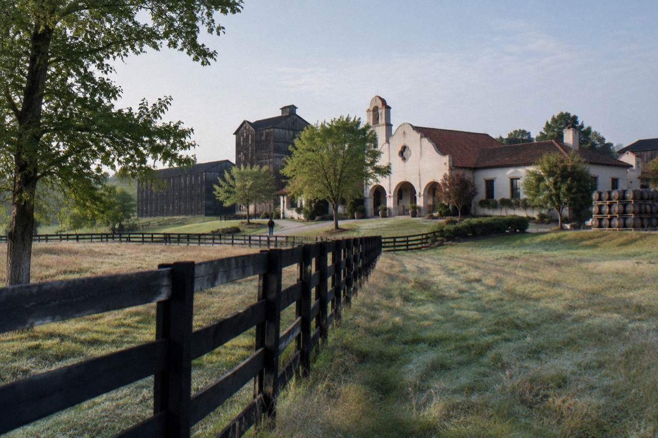 Rolling Kentucky farmland with a limestone distillery building and rickhouse barns in the background