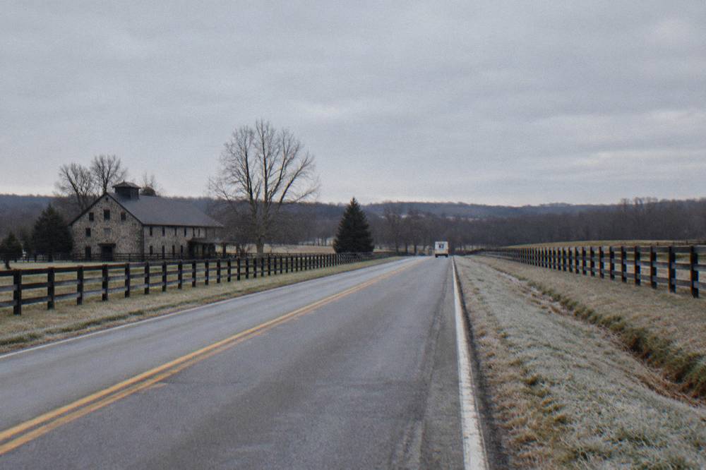 An empty two-lane country road lined with black wooden fences under a wide sky in rural Kentucky.