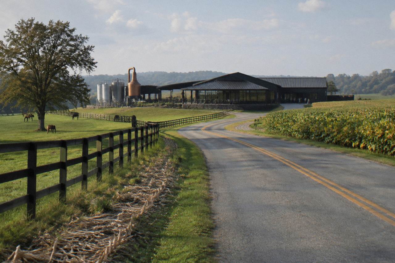 A country road curving past fenced horse pasture toward a limestone distillery building in central Kentucky.