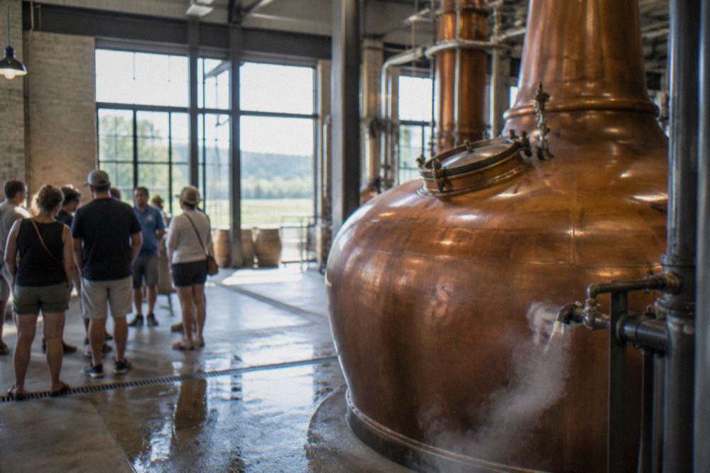 A small tour group standing beside a copper pot still inside a distillery