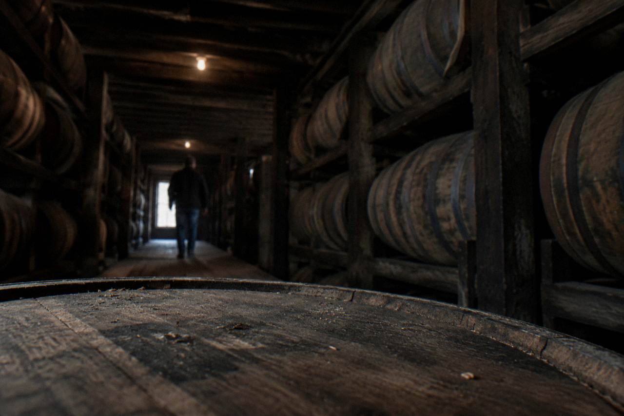 A row of bourbon barrels aging inside a dimly lit Kentucky rickhouse