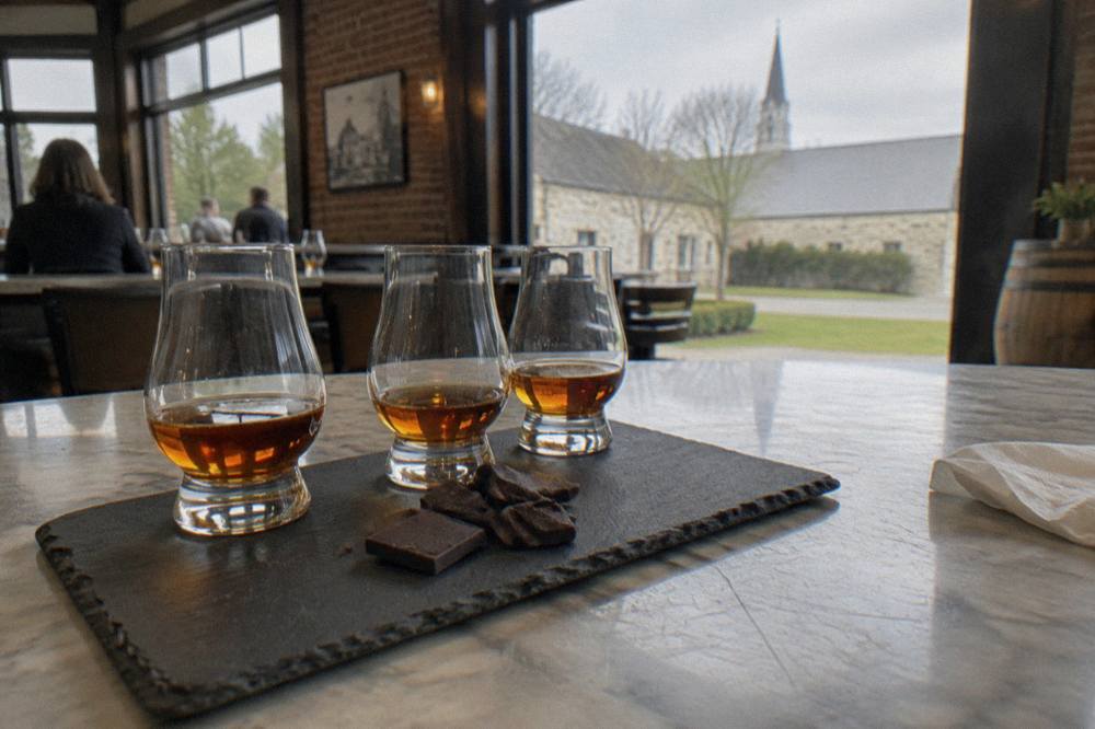 A tasting flight of bourbon in small glasses beside chocolate pieces on a distillery bar top