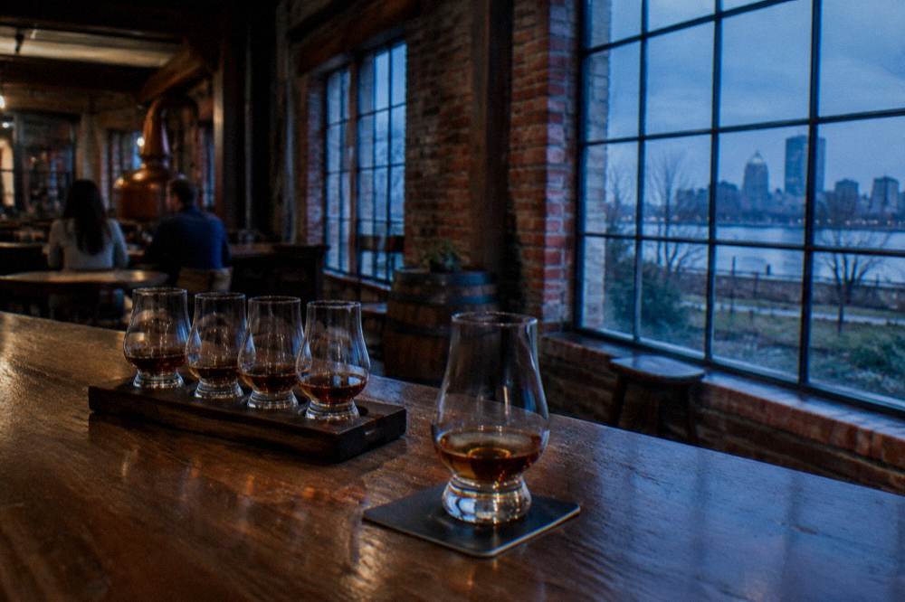 Glass of bourbon beside a tasting flight on a wooden distillery bar counter