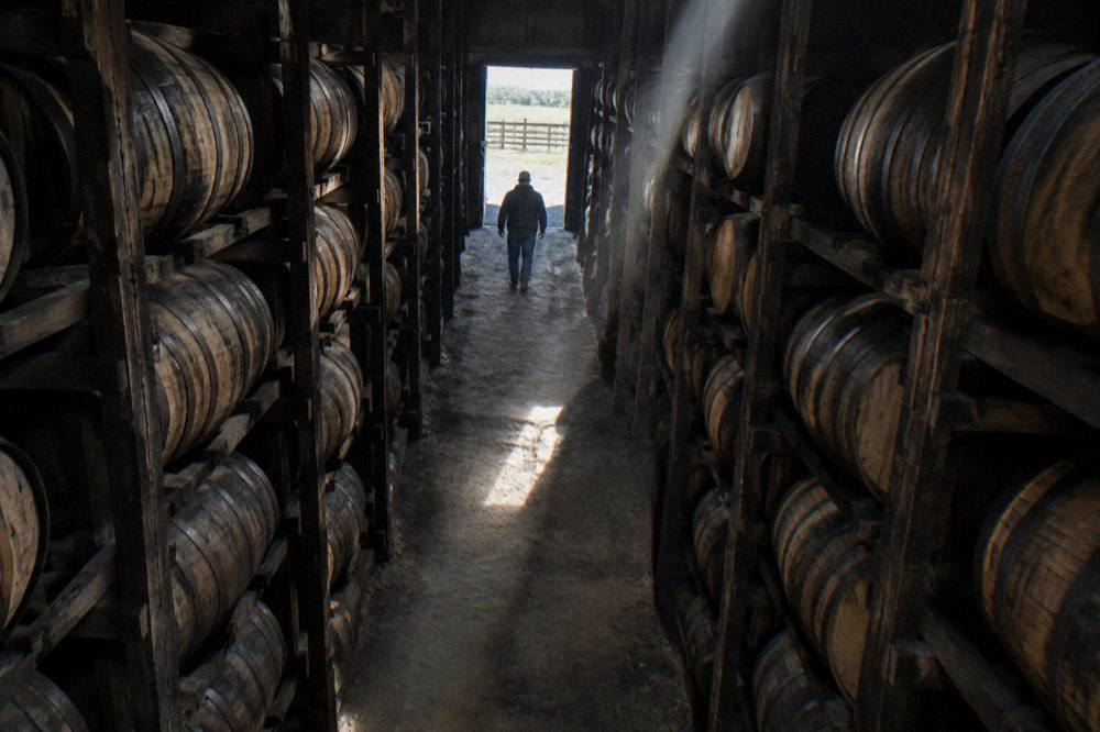 Rows of aging barrels stacked inside a dim bourbon rackhouse