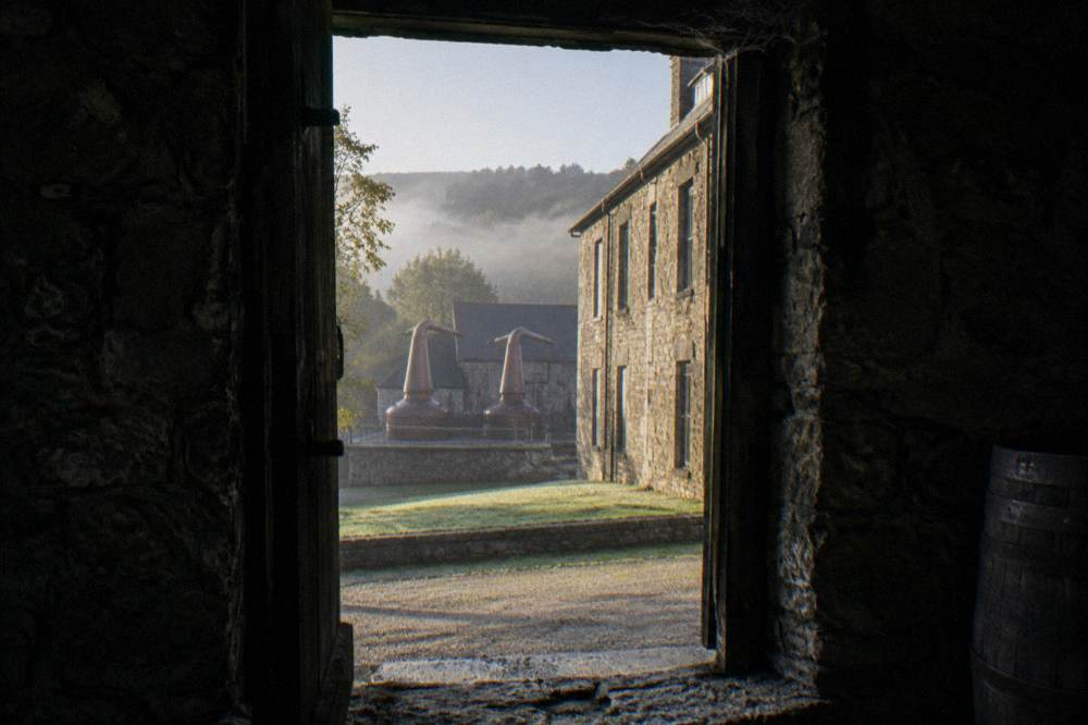 Stone distillery buildings and copper pot stills seen through a rickhouse doorway