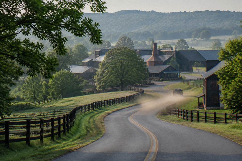 Winding rural road through green Kentucky hills toward a distillery campus