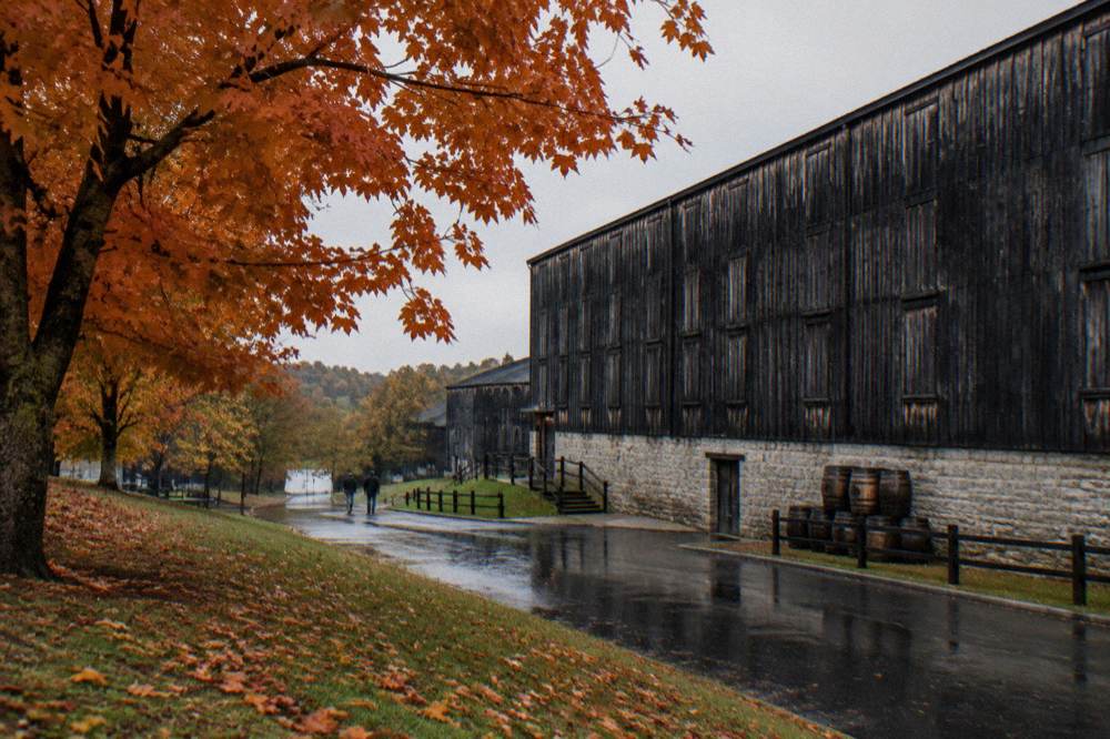 A barrel warehouse and stone distillery building surrounded by autumn foliage in Kentucky