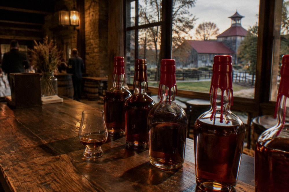 Wax-dipped bourbon bottles lined up on a wooden tasting bar in a distillery