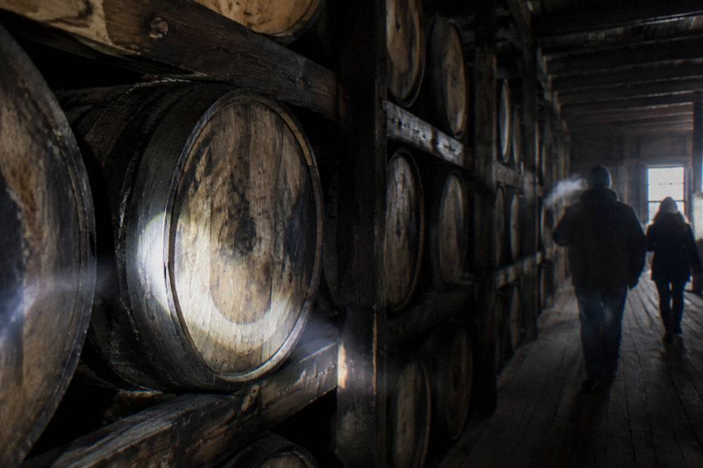 Rows of wooden bourbon barrels stacked inside a dim rickhouse