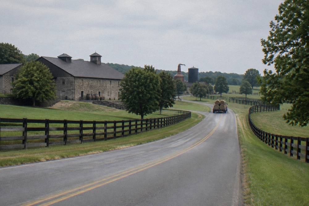 An empty two-lane country road winding past fenced horse pasture in central Kentucky