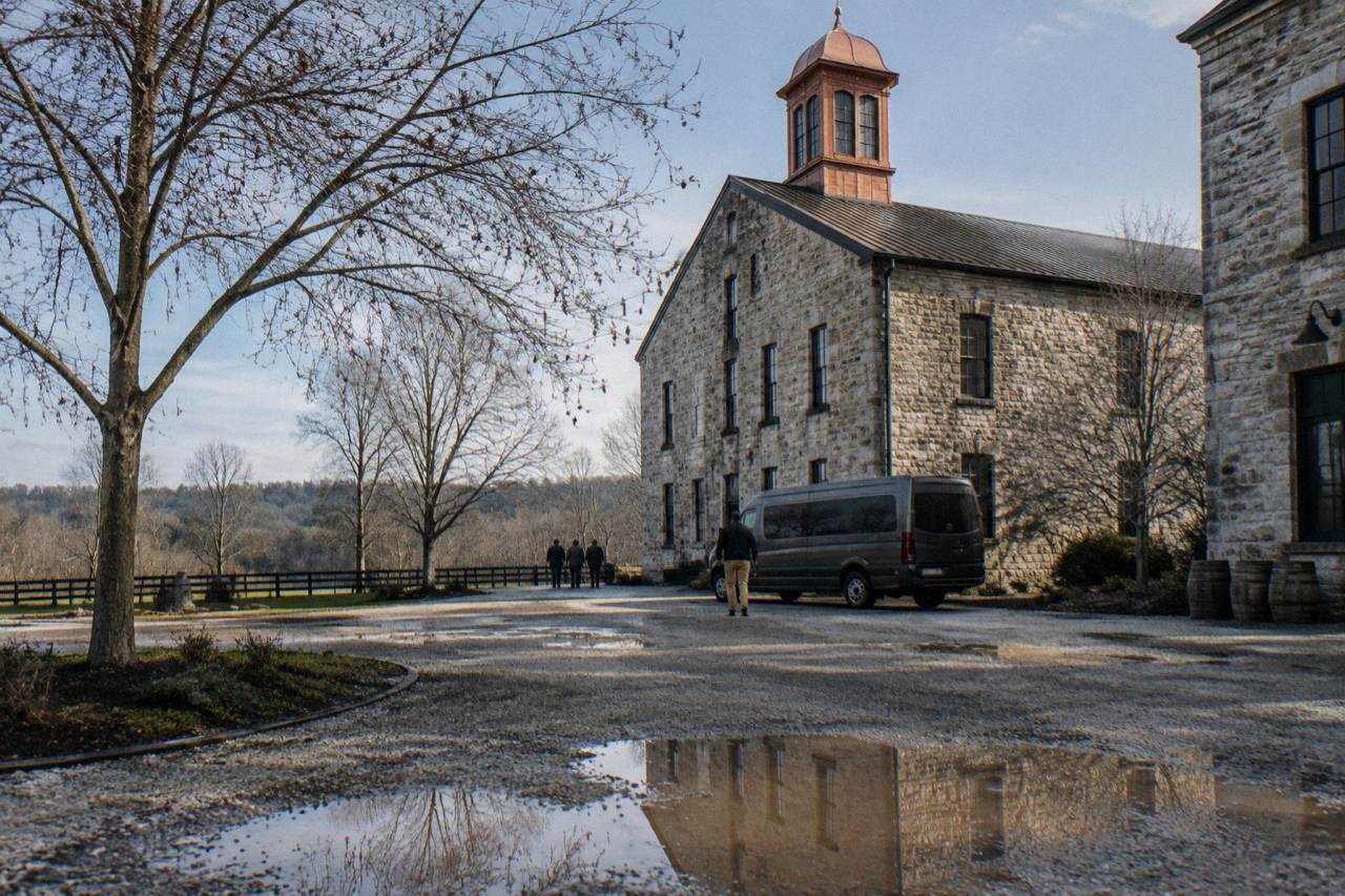 A passenger van parked on a country road beside a limestone distillery building in Kentucky
