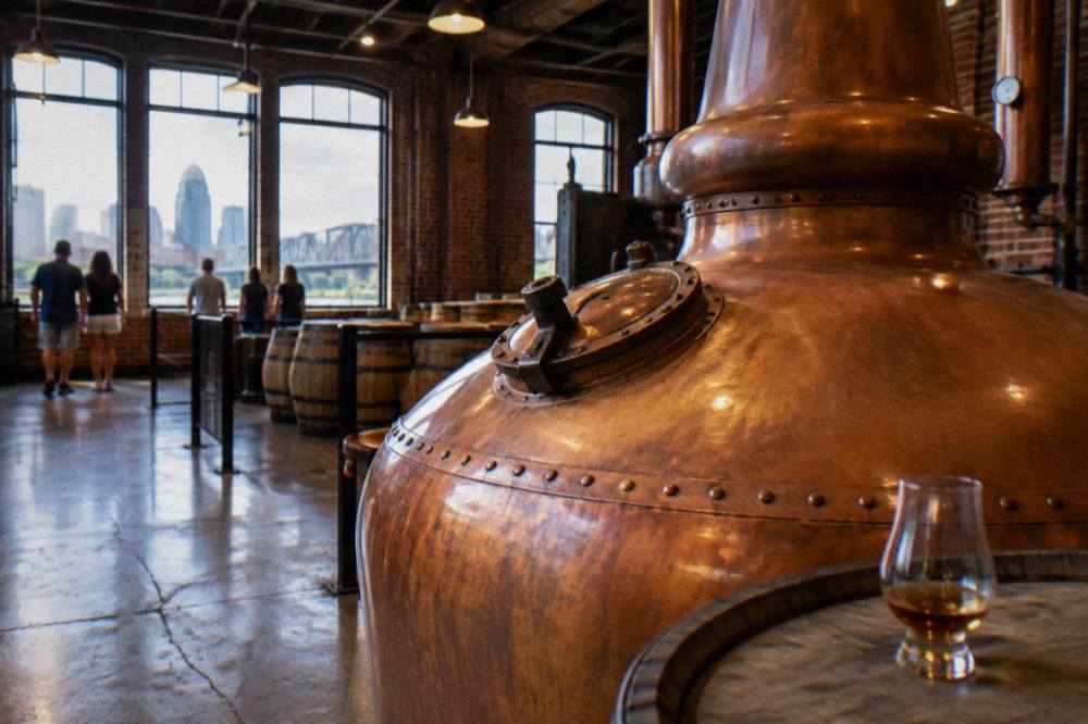 Copper pot still inside a craft bourbon distillery lit by warm industrial lighting