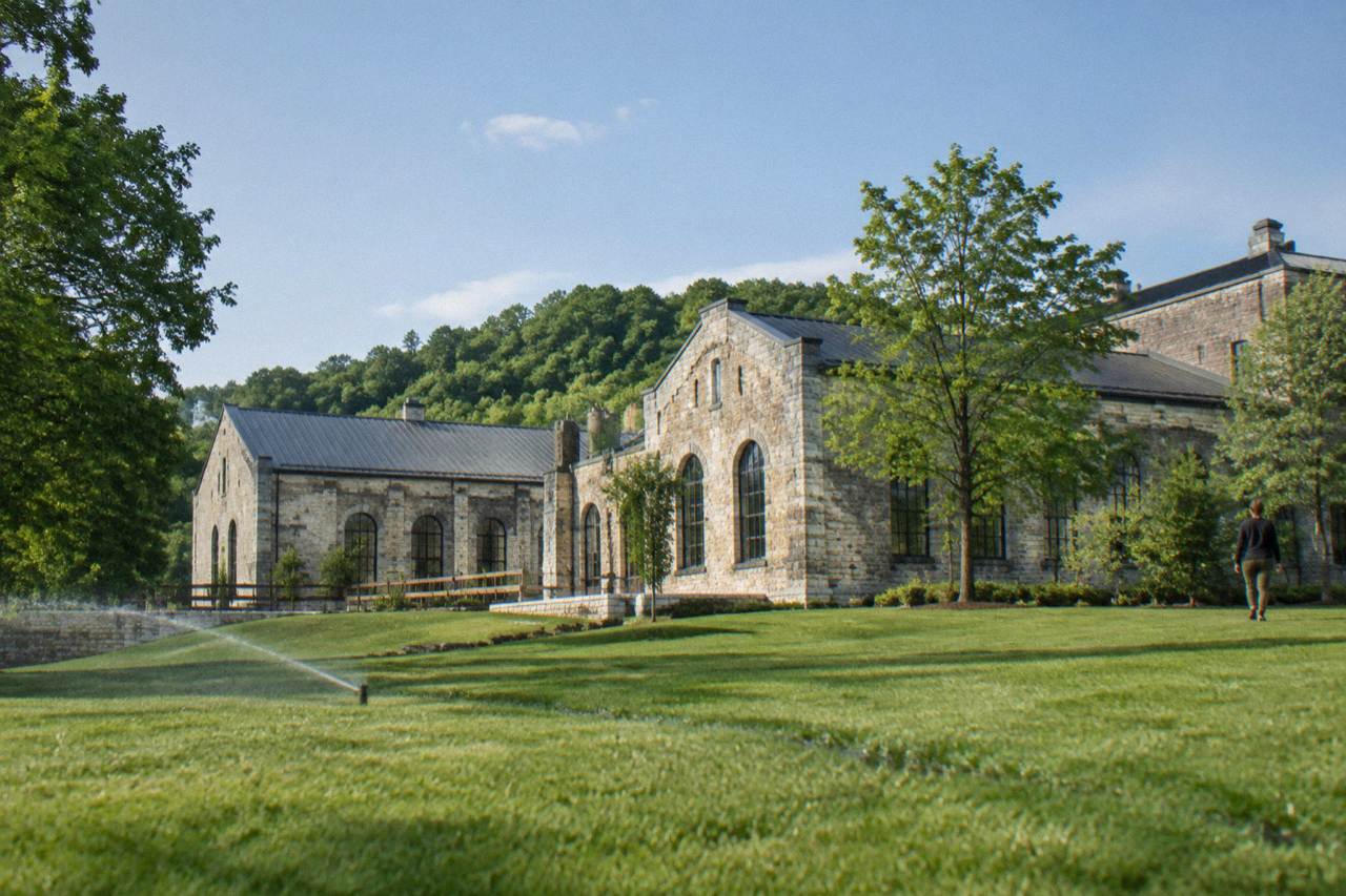 Historic limestone distillery buildings on a green Kentucky hillside under a wide sky