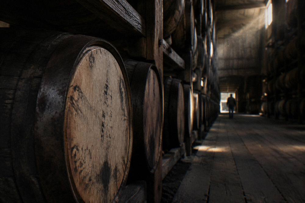 Row of charred oak bourbon barrels stacked inside a dim rickhouse