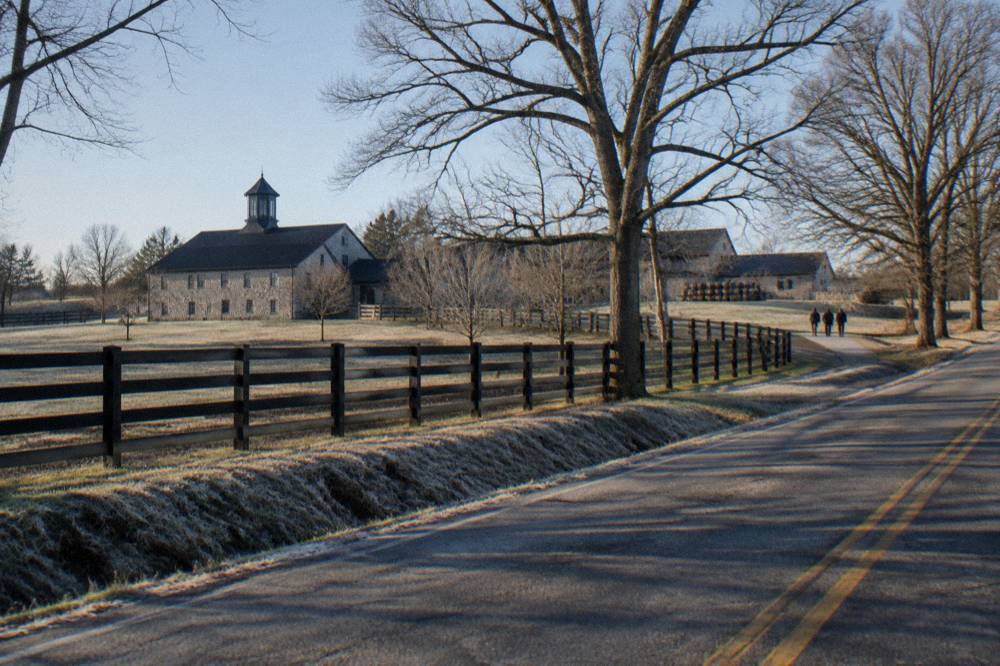Two-lane country road lined with black bourbon fences in central Kentucky
