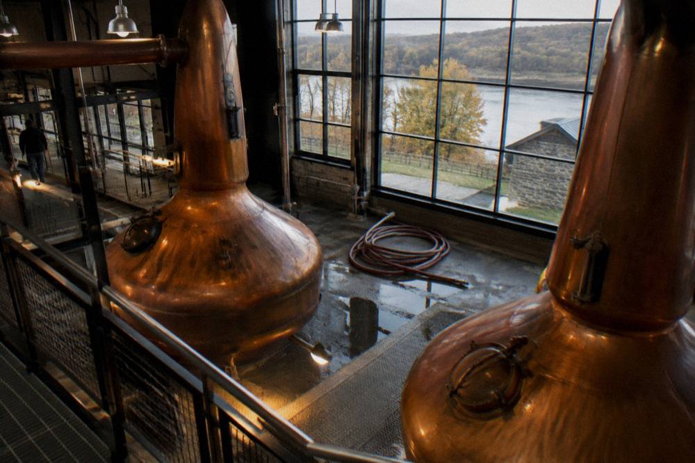Copper pot stills inside a working bourbon distillery with warm industrial lighting