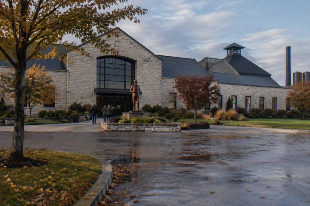 A wide limestone distillery building with a copper statue at the entrance