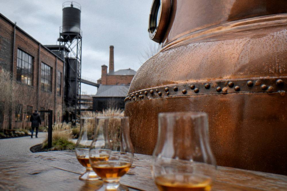 A copper pot still inside a small distillery with tasting glasses on a table in the foreground