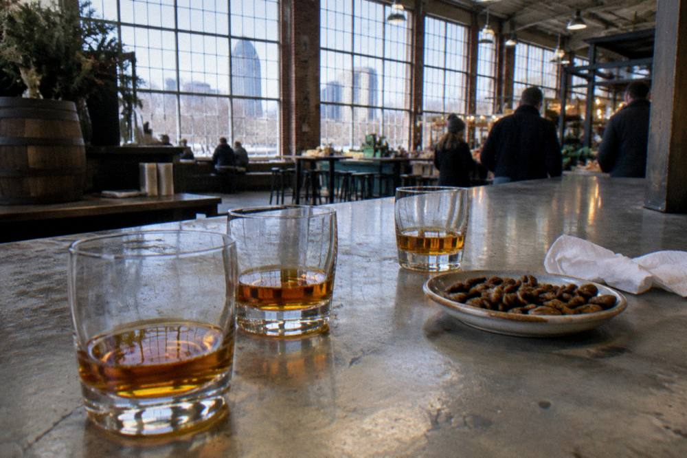 Glasses of amber bourbon lined on a bar counter beside a small tasting plate