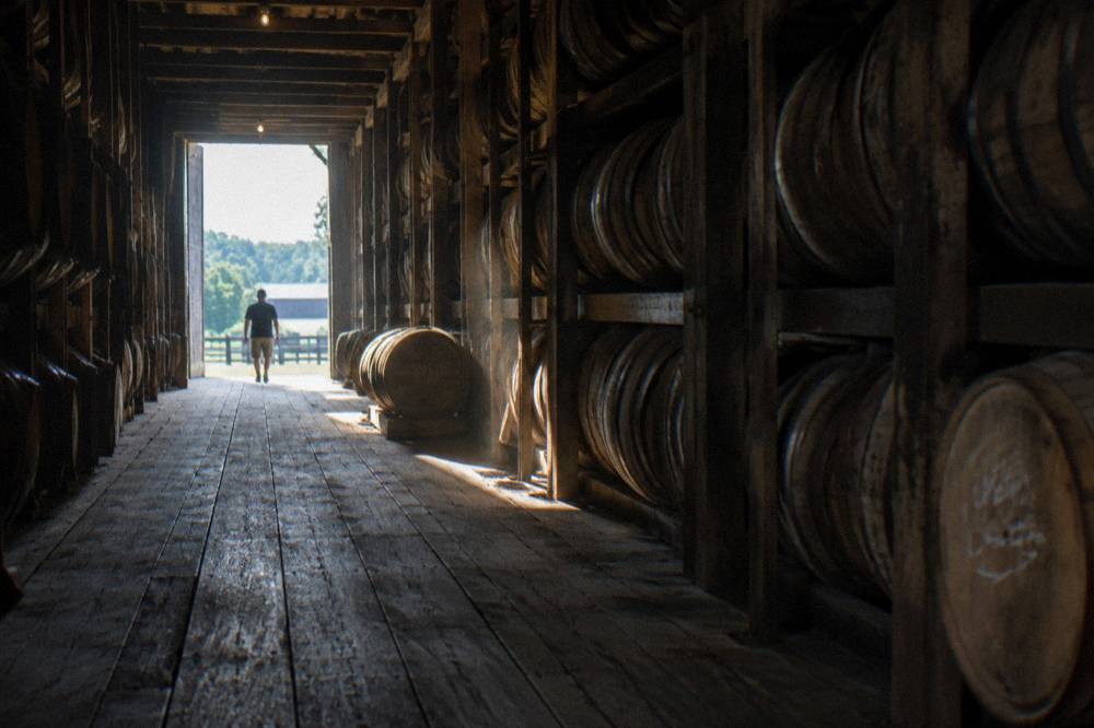 Bourbon barrels stacked in a Kentucky rickhouse with sunlight through the warehouse windows
