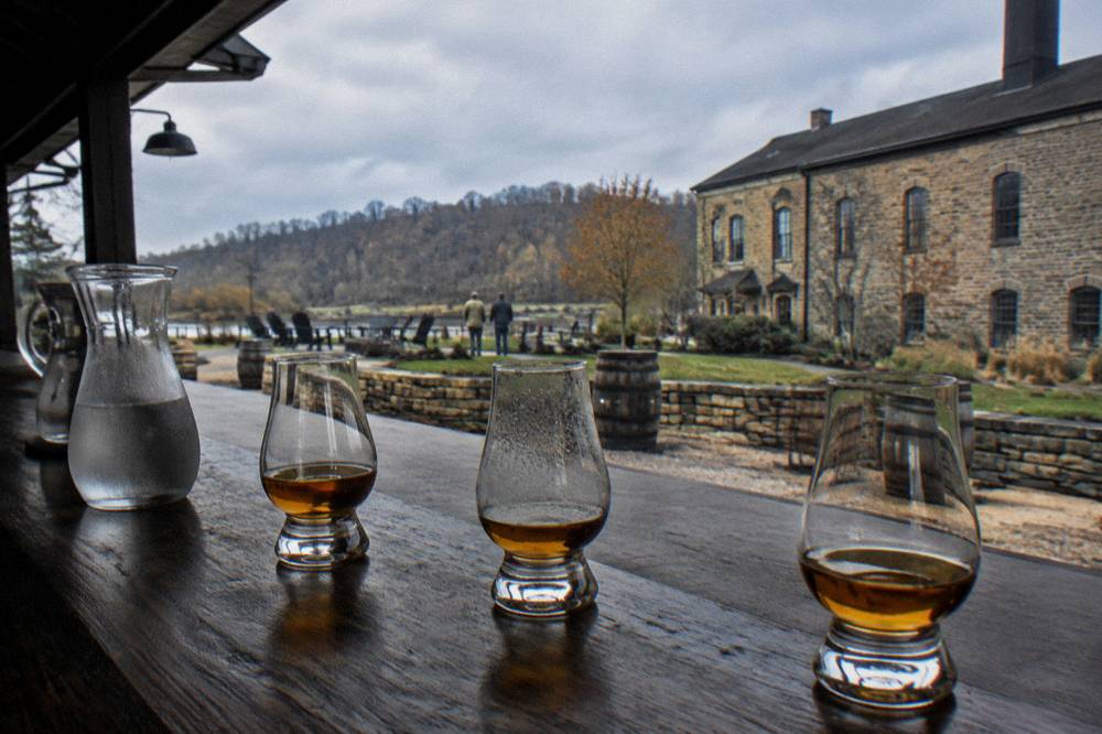 Tasting glasses of amber bourbon lined on a wooden bar top