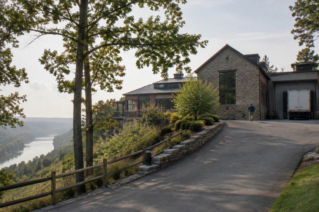 Hilltop distillery buildings with a limestone visitor center and wooded Kentucky hills behind