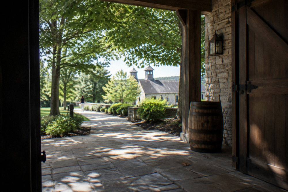 A covered stone porch and wooden doors of a historic distillery building surrounded by trees